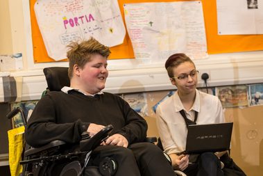 Two teenage boys sit smiling at the laptop in front of them.