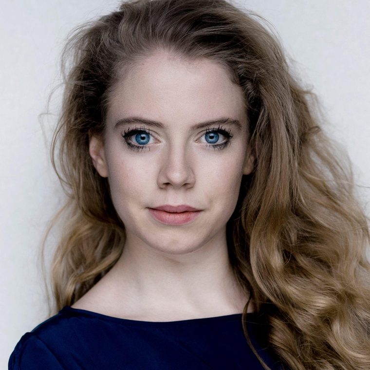 Meghan Tyler has large blue eyes and long, loosely curled blonde hair.