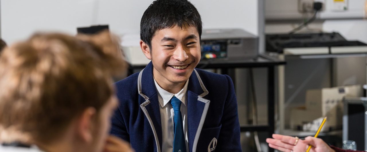 A teenage boy in a smart blue blazer smiles at the camera.